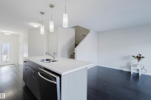 The kitchen features a contemporary island with a sink and a dishwasher, illuminated by three pendant lights - 2082 Price Landing, Edmonton, AB - Indoor Photo Showing Kitchen With Double Sink