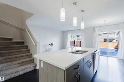 The property features a kitchen island with a double sink and pendant lighting, dark wood flooring, and sliding glass doors leading to the exterior - 2082 Price Landing, Edmonton, AB - Indoor Photo Showing Kitchen With Double Sink