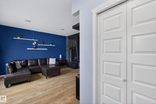 This living area features light-colored flooring, a contrasting blue wall with decorative shelving, and a dark stone-clad fireplace - 1522 Chapman Way, Edmonton, AB - Indoor