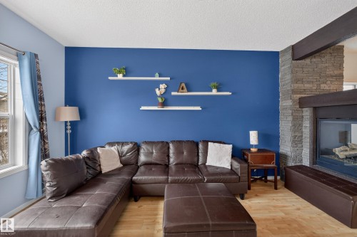 Living area featuring hardwood floors, a stone fireplace, and a window providing natural light - 1522 Chapman Way, Edmonton, AB - Indoor Photo Showing Living Room With Fireplace