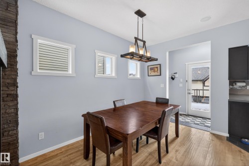 The dining area features light hardwood flooring, a dark wood dining table with seating for four, and an overhead chandelier - 1522 Chapman Way, Edmonton, AB - Indoor Photo Showing Dining Room