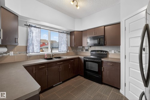 The kitchen features brown cabinetry, a black range, a built-in microwave, and a double basin sink - 1522 Chapman Way, Edmonton, AB - Indoor Photo Showing Kitchen With Double Sink