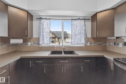 The kitchen features dark cabinetry, light countertops, and a double basin sink beneath a window - 1522 Chapman Way, Edmonton, AB - Indoor Photo Showing Kitchen With Double Sink