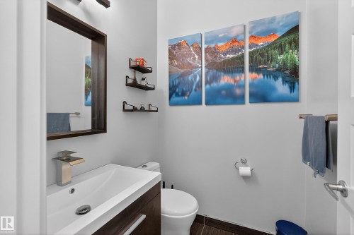 Bathroom featuring a vanity with an integrated sink and modern faucet, a wall-mounted mirror with a dark wood frame, and floating wall shelves - 1522 Chapman Way, Edmonton, AB - Indoor Photo Showing Bathroom