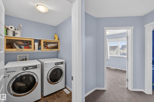 Dedicated laundry area with a white front-loading washer and dryer, a white shelf, and two light wood-framed storage cabinets - 1522 Chapman Way, Edmonton, AB - Indoor Photo Showing Laundry Room