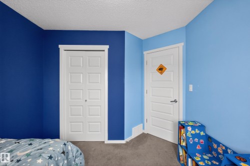 This room features two white doors with paneled detailing, grey carpeting, and walls painted in two tones of blue - 1522 Chapman Way, Edmonton, AB - Indoor Photo Showing Bedroom