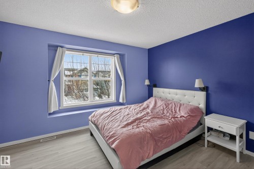 This bedroom features light wood-style flooring, a large window with white trim, and a ceiling light fixture - 1522 Chapman Way, Edmonton, AB - Indoor Photo Showing Bedroom