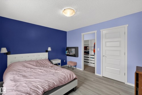 The bedroom features plank flooring, a white headboard, and wall-mounted light fixtures - 1522 Chapman Way, Edmonton, AB - Indoor Photo Showing Bedroom