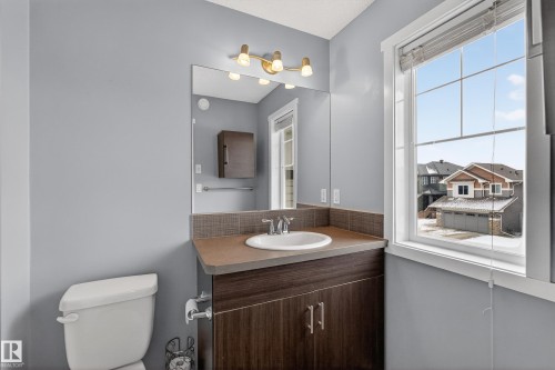 The bathroom features a vanity with a white sink, a mirror, and a window providing natural light - 1522 Chapman Way, Edmonton, AB - Indoor Photo Showing Bathroom