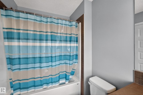 The bathroom features a white bathtub with a shower curtain, a toilet, and light gray painted walls - 1522 Chapman Way, Edmonton, AB - Indoor Photo Showing Bathroom