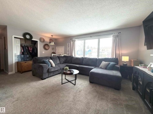 The living area features light-colored carpeting, light grey walls, and a large window providing natural light - 3912 108 Street, Edmonton, AB - Indoor Photo Showing Living Room