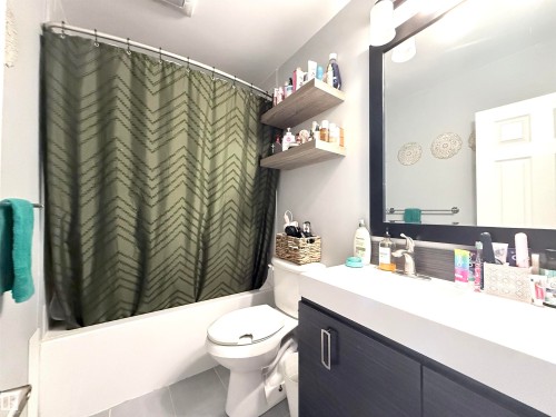 The bathroom features a vanity with a white countertop and dark cabinetry, a framed mirror, and a bathtub with a shower curtain - 3912 108 Street, Edmonton, AB - Indoor Photo Showing Bathroom