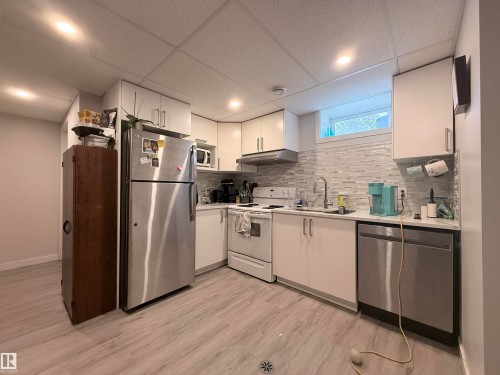 The kitchen features white cabinetry, a light-colored tile backsplash, and stainless steel appliances, including a refrigerator and dishwasher - 3912 108 Street, Edmonton, AB - Indoor Photo Showing Kitchen