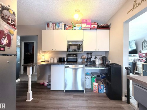 The kitchen features white cabinetry, dark countertops, a stainless steel dishwasher, and wood-look flooring - 3912 108 Street, Edmonton, AB - Indoor Photo Showing Kitchen