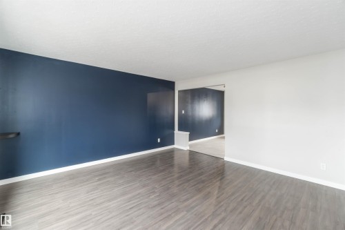 Living space featuring a striking dark blue accent wall, lighter walls, and wood-look flooring - 12121 38 Street, Edmonton, AB - Indoor Photo Showing Other Room