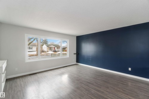 Living area featuring a spacious window, dark wood-style flooring, a dark blue accent wall, and light-colored walls - 12121 38 Street, Edmonton, AB - Indoor Photo Showing Living Room