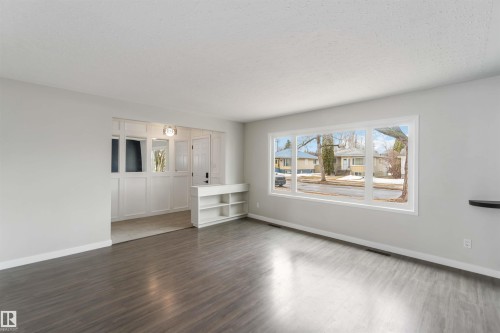 Spacious living area featuring large windows, dark wood-style flooring, and a built-in shelving unit - 12121 38 Street, Edmonton, AB - Indoor Photo Showing Other Room