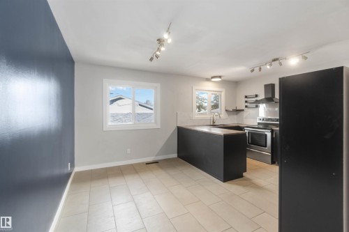 The property features a kitchen with dark cabinetry, stainless steel appliances including a range and hood, and tiled flooring - 12121 38 Street, Edmonton, AB - Indoor Photo Showing Kitchen