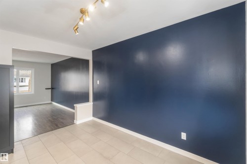 The property offers a room with a dark blue accent wall, neutral-toned floor tiles, and a contemporary track lighting fixture - 12121 38 Street, Edmonton, AB - Indoor Photo Showing Other Room