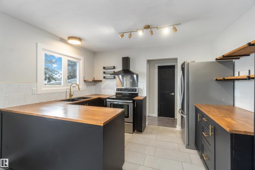 The kitchen features wood countertops, dark cabinetry with gold-toned hardware, a stainless steel refrigerator, and a stainless steel oven with an overhead range hood - 12121 38 Street, Edmonton, AB - Indoor Photo Showing Kitchen With Double Sink