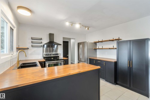 The kitchen features dark cabinetry with contrasting wood countertops, a stainless steel range with a matching hood, and a stainless steel refrigerator - 12121 38 Street, Edmonton, AB - Indoor Photo Showing Kitchen With Double Sink