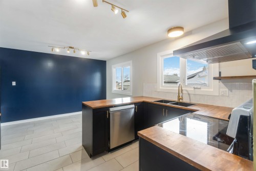 The property features a kitchen with dark cabinetry, wooden countertops, and a stainless steel dishwasher - 12121 38 Street, Edmonton, AB - Indoor Photo Showing Kitchen With Double Sink