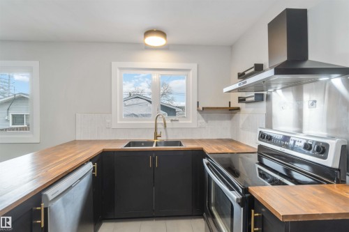 The kitchen features wooden countertops, black cabinetry with gold hardware, and a stainless steel oven and range hood - 12121 38 Street, Edmonton, AB - Indoor Photo Showing Kitchen With Double Sink