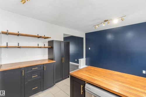 The kitchen features dark cabinetry with gold hardware, wood countertops, open shelving, and a track lighting fixture - 12121 38 Street, Edmonton, AB - Indoor Photo Showing Garage