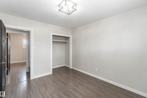 This room features wood-look flooring, a closet with a built-in shelf and hanging rod, and a modern ceiling light fixture - 12121 38 Street, Edmonton, AB - Indoor Photo Showing Other Room