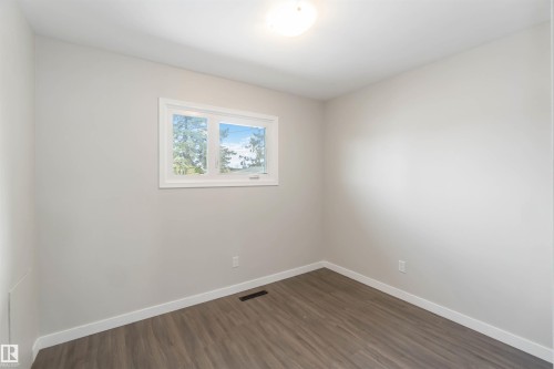 This room features light-toned walls, wood-style flooring, a window offering natural light, and a ceiling-mounted light fixture - 12121 38 Street, Edmonton, AB - Indoor Photo Showing Other Room