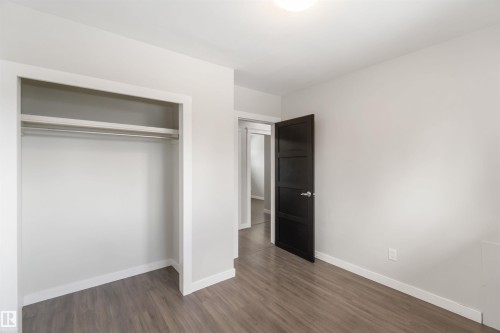This room features light-colored walls, wood-style flooring, and a dark paneled door - 12121 38 Street, Edmonton, AB - Indoor Photo Showing Other Room