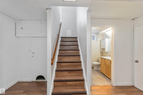 The interior features wood flooring, a wooden staircase with a handrail, and a bathroom with a window, toilet, and vanity with storage - 12121 38 Street, Edmonton, AB - Indoor Photo Showing Other Room