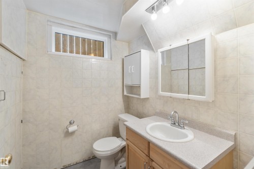 Bathroom featuring tiled walls, a vanity with a countertop and sink, a mirror, and a window - 12121 38 Street, Edmonton, AB - Indoor Photo Showing Bathroom