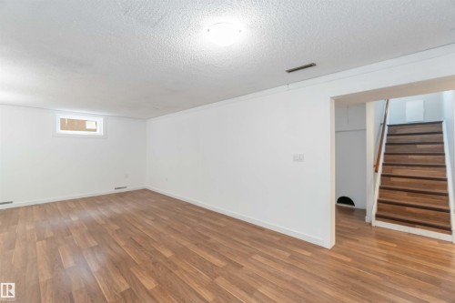 Spacious room featuring wood-look flooring, white walls, and a window providing natural light - 12121 38 Street, Edmonton, AB - Indoor Photo Showing Other Room