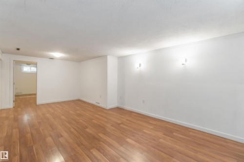 Spacious room featuring hardwood flooring, white walls, and overhead lighting, with additional wall sconces providing ambient illumination - 12121 38 Street, Edmonton, AB - Indoor Photo Showing Other Room