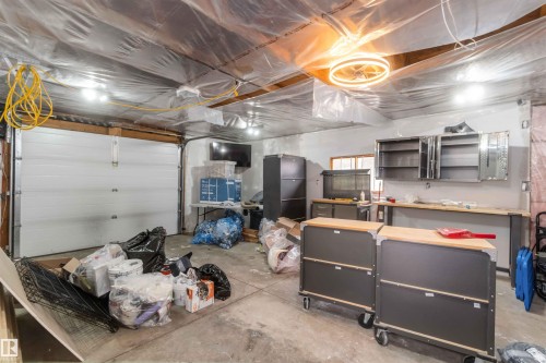 The property features a garage with a roll-up door, exposed ceiling joists, and concrete flooring - 12121 38 Street, Edmonton, AB - Indoor Photo Showing Garage
