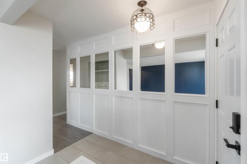 Entryway featuring a decorative pendant light fixture, white wainscoting, and a paneled white door with black hardware - 12121 38 Street, Edmonton, AB - Indoor Photo Showing Other Room