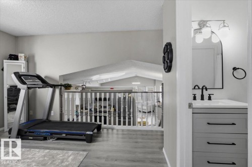 The property features a spacious loft area with light gray flooring and a white railing, overlooking an area with vaulted ceilings - 5837 162A Avenue, Edmonton, AB - Indoor Photo Showing Gym Room