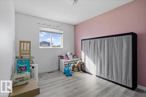 The room features light wood-style flooring, a window offering natural light, and walls with a two-tone paint scheme - 5837 162A Avenue, Edmonton, AB - Indoor Photo Showing Bedroom