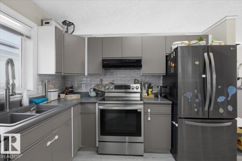The kitchen features grey cabinetry, stainless steel appliances, a double basin sink with a gooseneck faucet, and a tiled backsplash - 5837 162A Avenue, Edmonton, AB - Indoor Photo Showing Kitchen With Double Sink