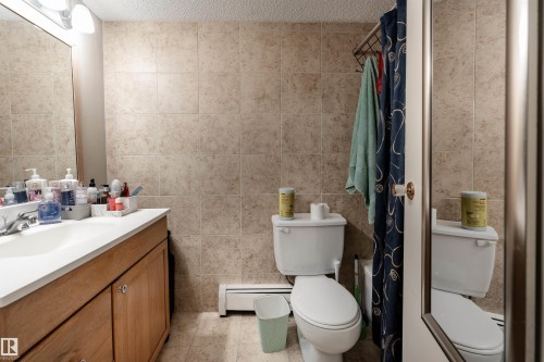 Bathroom featuring a wooden vanity with a white countertop and an integrated sink, a toilet, and tiled walls - 2 10737 116 Street, Edmonton, AB - Indoor Photo Showing Bathroom