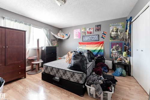 This room features light wood-style flooring, a window with curtains, and a dark wood wardrobe - 2 10737 116 Street, Edmonton, AB - Indoor Photo Showing Bedroom