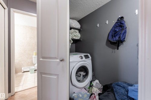 Dedicated laundry area featuring a front-loading washing machine and wall-mounted shelving - 2 10737 116 Street, Edmonton, AB - Indoor Photo Showing Laundry Room