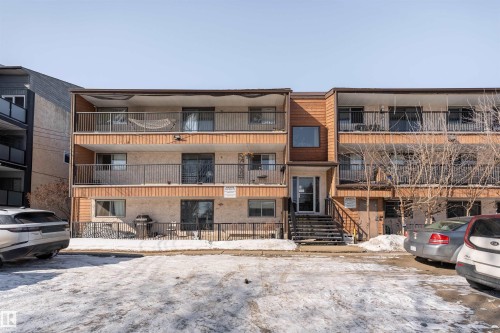 Exterior view of a three-story property featuring balconies with dark railings, a prominent entrance with stairs, and a mix of wood and light-colored siding - 2 10737 116 Street, Edmonton, AB - Outdoor