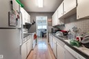 The kitchen features white cabinetry, a light grey subway tile backsplash, and wood-style flooring - 2 10737 116 Street, Edmonton, AB  - Indoor Photo Showing Kitchen 