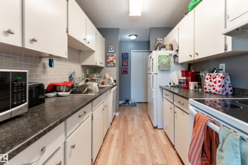 The kitchen features white cabinetry, dark countertops, and a subway tile backsplash - 2 10737 116 Street, Edmonton, AB - Indoor Photo Showing Kitchen