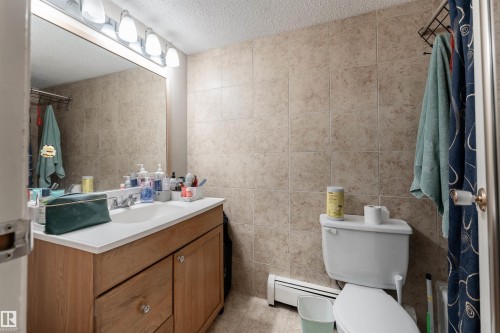 Bathroom featuring a vanity with wood cabinetry, a white countertop, and a large mirror - 2 10737 116 Street, Edmonton, AB - Indoor Photo Showing Bathroom