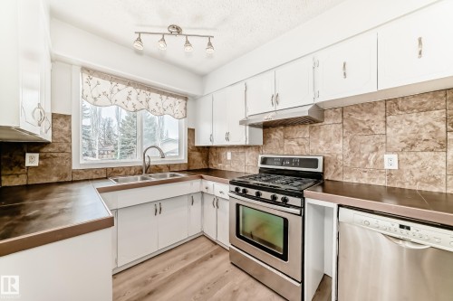 The kitchen features white cabinetry, stainless steel appliances, a double basin sink, and a tiled backsplash - 4312 43 Avenue, Leduc, AB - Indoor Photo Showing Kitchen With Double Sink