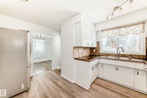 The kitchen features white cabinetry, a double basin sink, and a tiled backsplash, complemented by wood-look flooring - 4312 43 Avenue, Leduc, AB - Indoor Photo Showing Kitchen With Double Sink