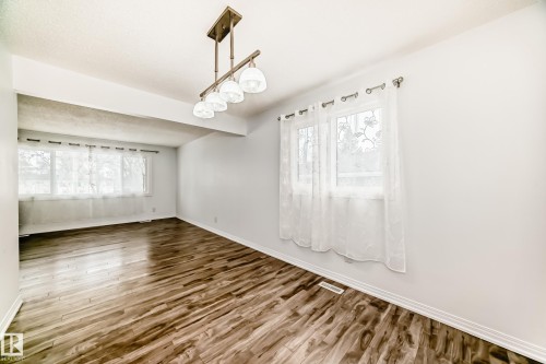 This interior space features wood-style flooring, white walls, and a ceiling-mounted light fixture with four glass shades - 4312 43 Avenue, Leduc, AB - Indoor Photo Showing Other Room